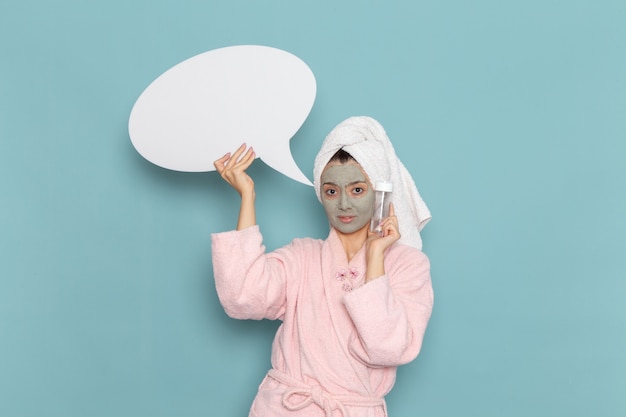 Front view young female in pink bathrobe after shower holding sign and spray on the blue wall beauty water cream selfcare shower bathroom