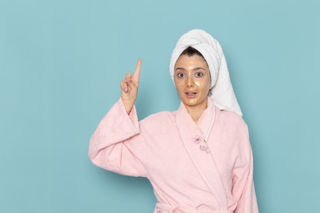 Front view young female in pink bathrobe after shower on light blue wall beauty water bath cream selfcare shower