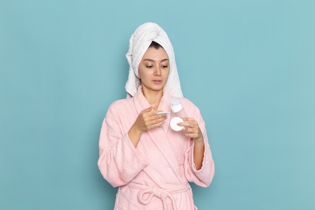 Вид спереди молодая женщина в розовом халате после душа на голубой стене, чистка красоты, чистая вода, крем для ухода за собой, душ