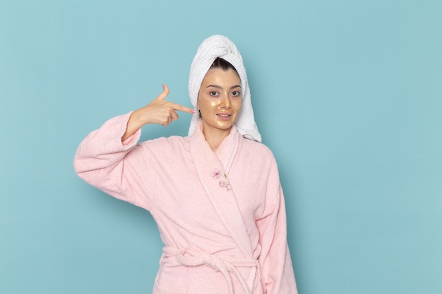 Front view young female in pink bathrobe after shower posing on blue wall cleaning beauty clean water selfcare cream shower