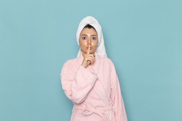 Front view young female in pink bathrobe after shower showing quiet sign on blue wall beauty water cream selfcare shower bathroom