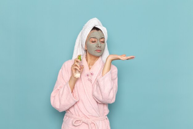 Front view young female in pink bathrobe after shower using spray on light-blue wall beauty clean water selfcare shower