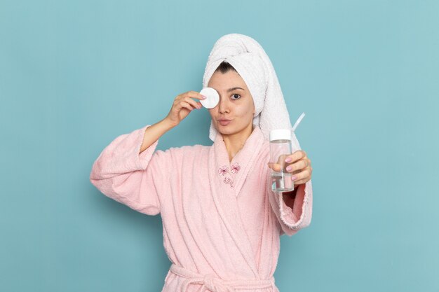뷰티 셀프 케어 크림을 청소하는 파란색 벽 샤워에 메이크업에서 그녀의 얼굴을 청소 분홍색 목욕 가운에 전면보기 젊은 여성