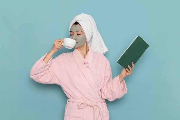 커피를 마시고 파란색 벽 청소 뷰티 셀프 케어 크림 샤워에 카피 북을 읽고 분홍색 목욕 가운에 전면보기 젊은 여성