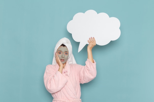 Free photo front view young female in pink bathrobe holding big white sign on blue wall cleaning beauty selfcare cream shower