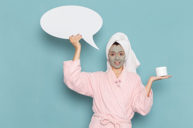 front view young female in pink bathrobe holding white sign and cream on blue wall beauty water bath cream selfcare shower