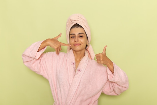 Free photo front view young female in pink bathrobe posing and smiling on a green surface