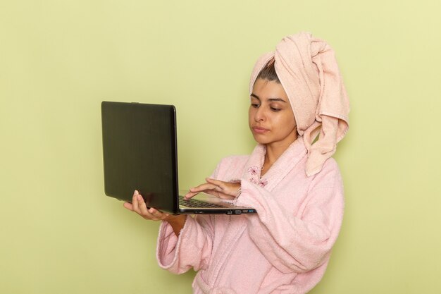 녹색 표면에 노트북을 사용하는 분홍색 목욕 가운에 전면보기 젊은 여성