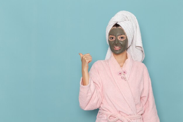 Front view young female in pink bathrobe with mask on her face on blue wall shower cleaning beauty self-care cream