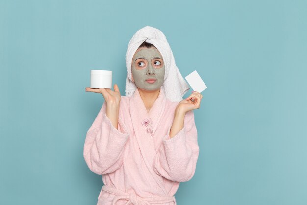 正面図ピンクのバスローブを着た若い女性の顔にマスクを持って青い壁のシャワーのクリーニング美容セルフケアクリーム
