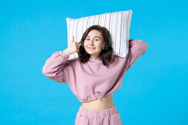 青い壁に枕を保持しているピンクのパジャマの正面図若い女性夜の色不眠症睡眠ベッド安静夢のパーティーの感情