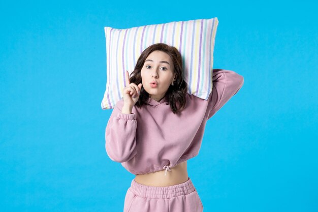 青い壁に枕を保持しているピンクのパジャマの正面図若い女性夜の色不眠症睡眠ベッド安静夢の女性の感情