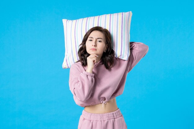 青い壁に枕を保持しているピンクのパジャマの正面図若い女性夜の色不眠症睡眠ベッド安静夢の女性パーティーの感情