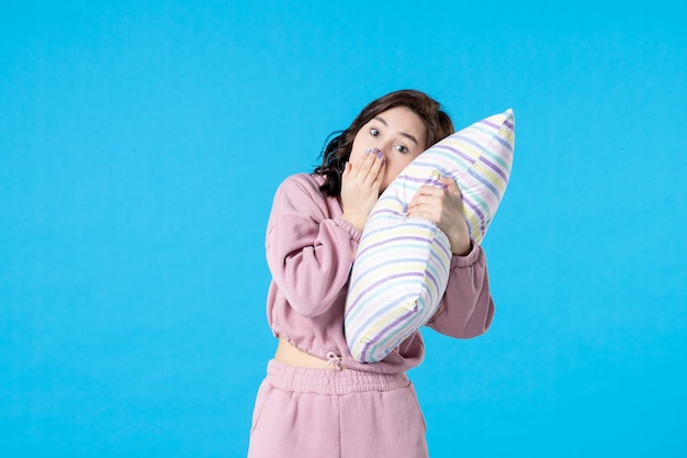 Вид спереди молодая женщина в розовой пижаме, держащая подушку на синей стене, ночь, цвет, вечеринка, бессонница, постельный режим, сон, эмоция, сон