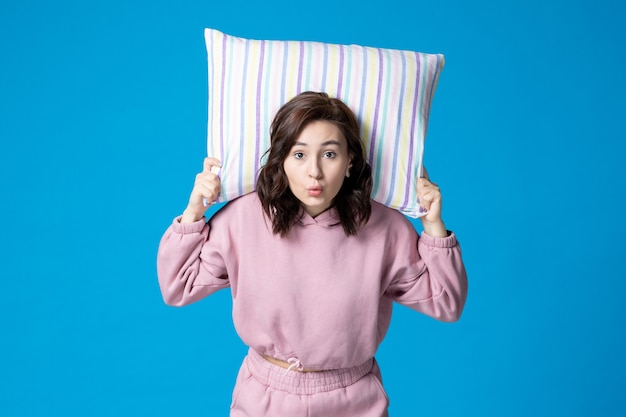 Front view young female in pink pajamas holding pillow on blue wall night color sleep bed rest emotion dream insomnia party