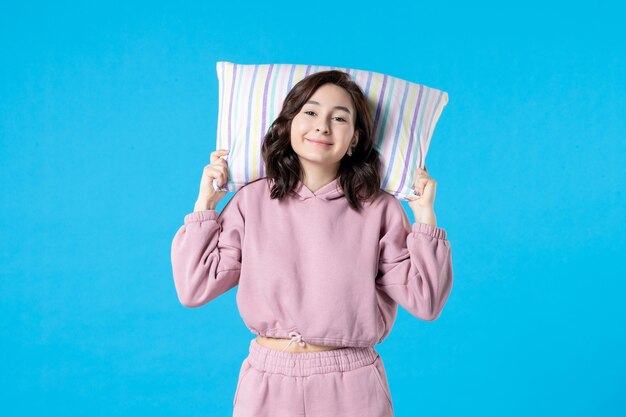 Front view young female in pink pajamas holding pillow on blue wall night color sleep bed rest emotion dream woman insomnia party