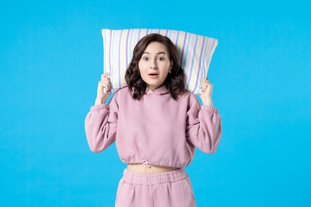 Front view young female in pink pajamas holding pillow on blue wall night color sleep bed rest emotion woman insomnia party