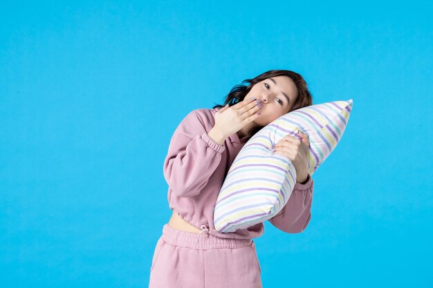 Front view young female in pink pajamas holding pillow close to her head on blue wall night color party insomnia bed rest woman sleep