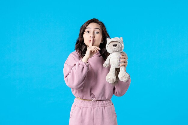 Front view young female in pink pajamas with little toy bear on blue color night sleep insomnia dream bed woman party rest quiet