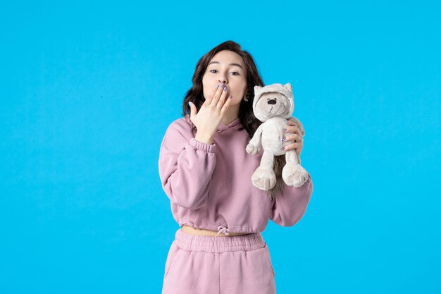 Front view young female in pink pajamas with little toy bear on blue color night sleep insomnia dream bed woman rest