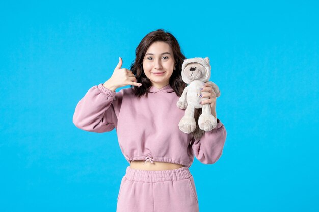 Front view young female in pink pajamas with little toy bear on blue color 