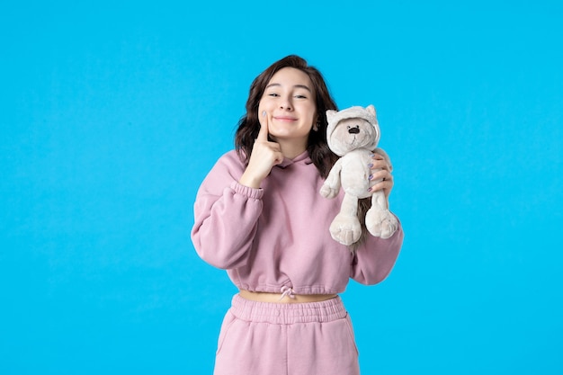 Front view young female in pink pajamas with little toy bear on blue dream color night sleep bed woman party rest