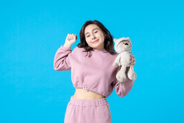 Front view young female in pink pajamas with little toy bear on blue dream color night sleep insomnia bed woman party