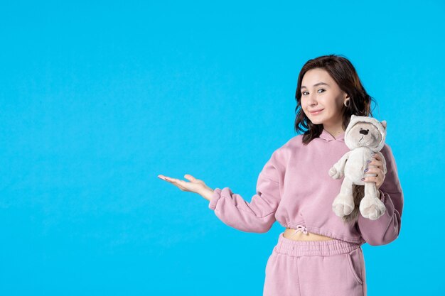 Front view young female in pink pajamas with little toy bear on blue dream color sleep bed party rest insomnia woman