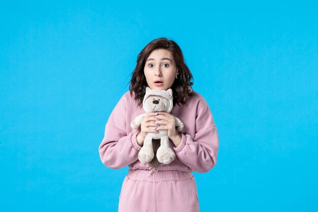 Front view young female in pink pajamas with little toy bear on blue