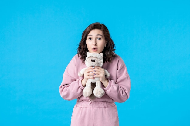 Front view young female in pink pajamas with little toy bear on blue