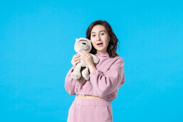 Front view young female in pink pajamas with little toy bear on blue