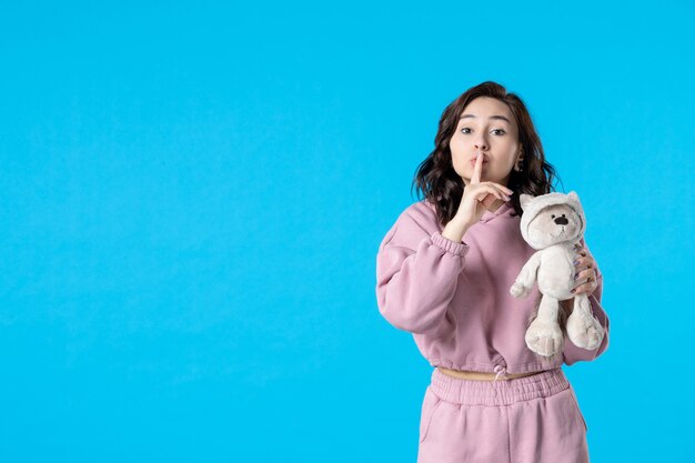 Front view young female in pink pajamas with little toy bear on blue