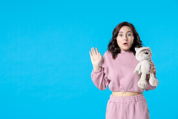 Front view young female in pink pajamas with little toy bear on blue