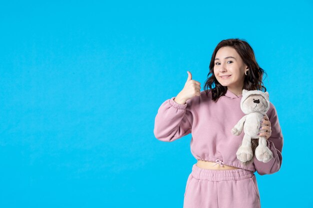 Front view young female in pink pajamas with little toy bear on blue