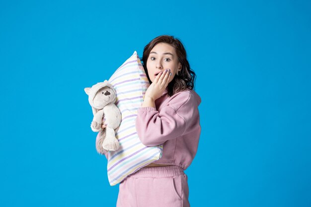 Front view young female in pink pajamas with little toy bear and pillow on blue bed night nightmare sleep woman rest dream party