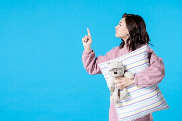 Front view young female in pink pajamas with little toy bear and pillow on blue insomnia bed night dream party rest sleep