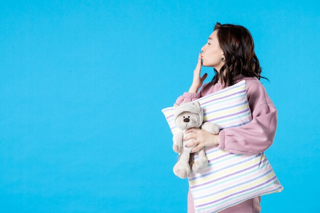 Front view young female in pink pajamas with little toy bear and pillow on blue insomnia bed night nightmare party rest sleep