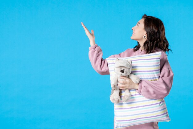 Front view young female in pink pajamas with little toy bear and pillow on blue woman