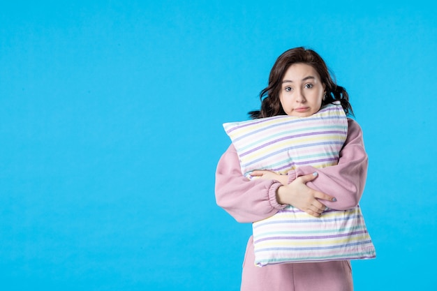 Вид спереди молодая женщина в розовой пижаме с подушкой на синем