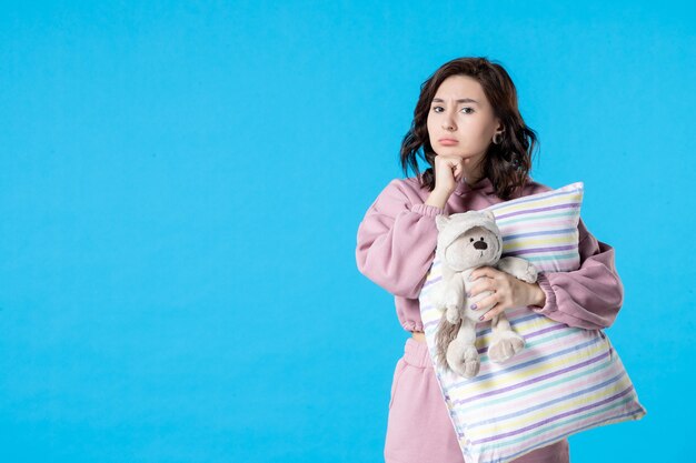 Вид спереди молодая женщина в розовой пижаме с игрушечным медведем и подушкой на синей ночи