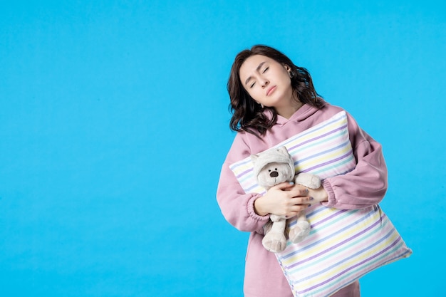 Foto gratuita vista frontale giovane donna in pigiama rosa con orsetto giocattolo e cuscino sulla notte blu