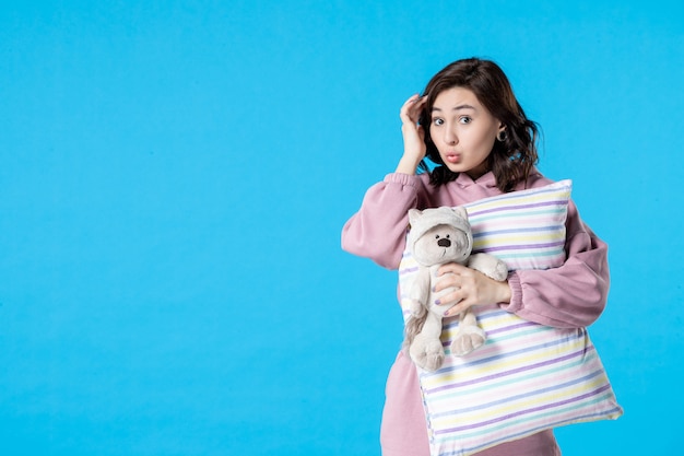 Front view young female in pink pajamas with toy bear and pillow on blue