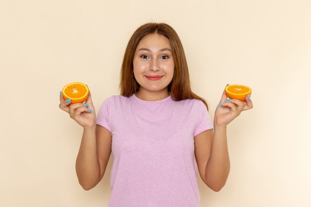 ピンクのtシャツと笑顔でオレンジ色を保持しているブルージーンズの正面の若い女性