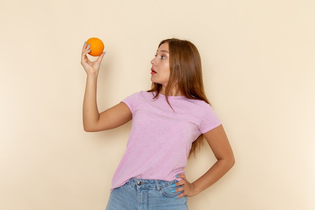 ピンクのtシャツとオレンジを保持しているブルージーンズの正面の若い女性