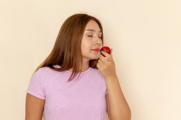 Front view young female in pink t-shirt and blue jeans holding smelling sour plum