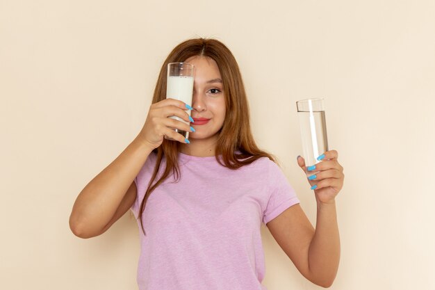 Вид спереди молодой женщины в розовой футболке и синих джинсах, держащей воду и молоко на сером
