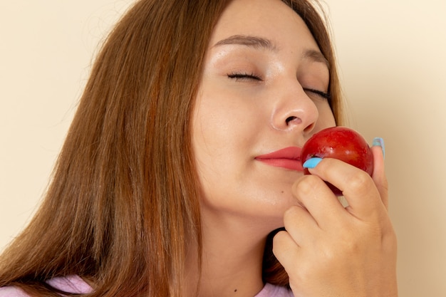 Front view young female in pink t-shirt and blue jeans smelling sour plum on grey