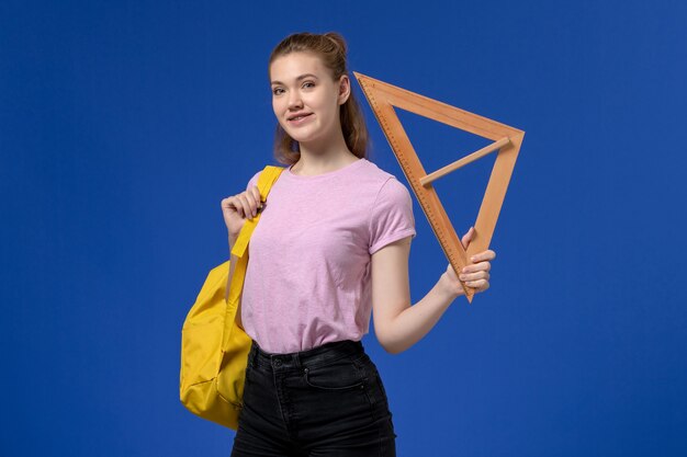 Вид спереди молодой женщины в розовой футболке, держащей деревянную треугольную фигуру на синей стене