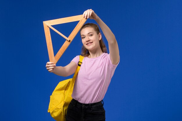 파란색 벽에 웃 고 나무 삼각형 그림을 들고 분홍색 티셔츠에 젊은 여성의 전면보기