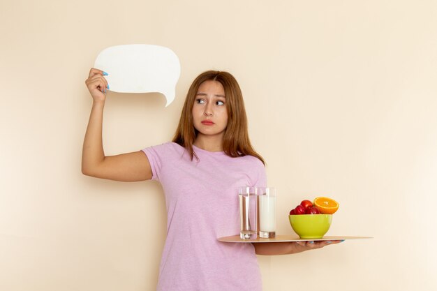 Front view young female in pink t-shirt and jeans holding tray fruits milk and water on grey
